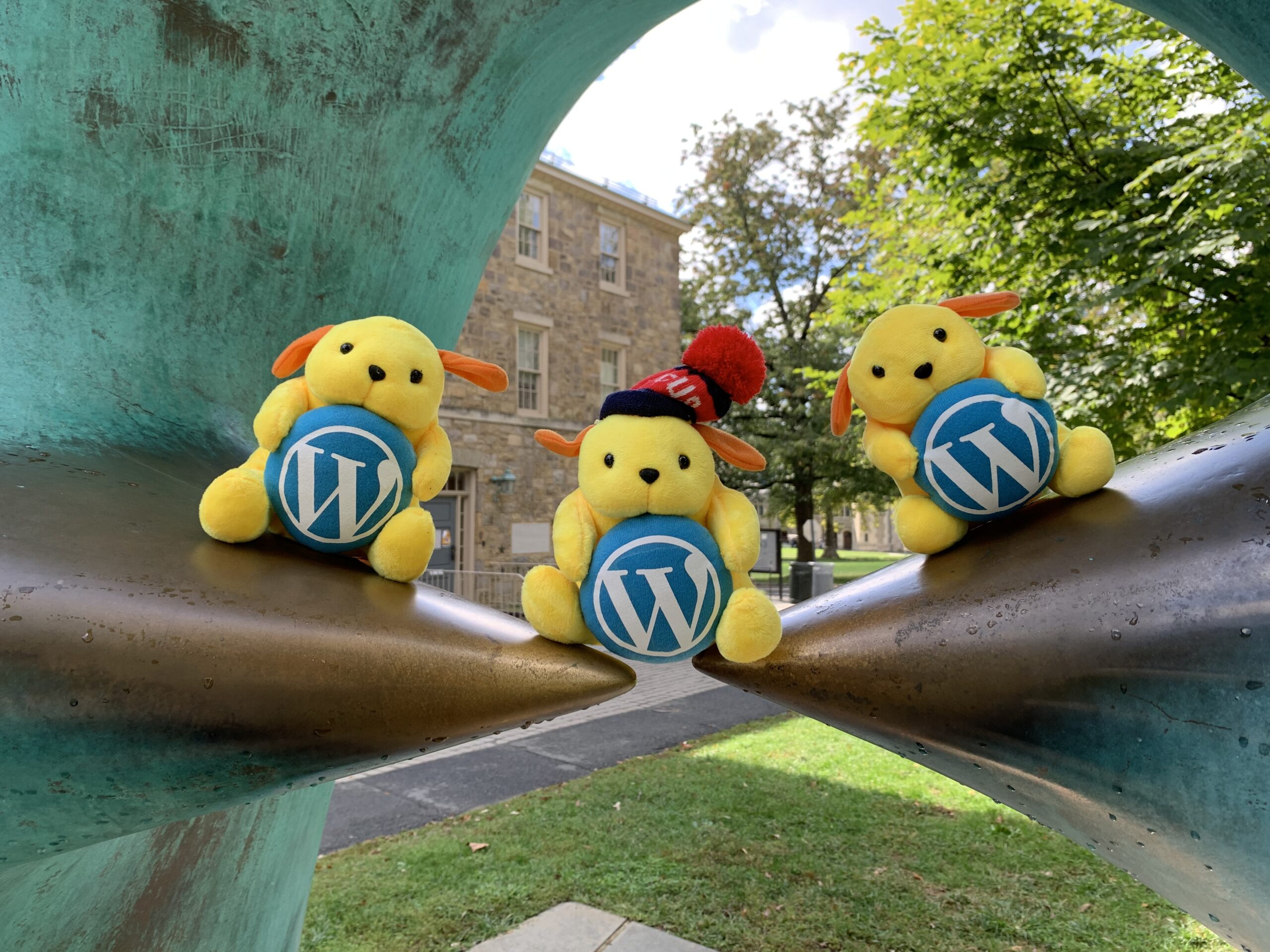 3 stuffed WordPress mascots sitting on the Oval with Points sculpture